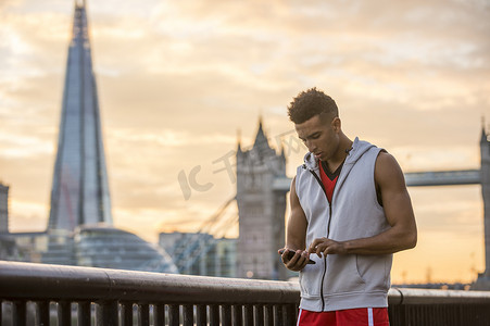 肌肉真人摄影照片_伦敦沃平一名男子在河边塔桥和背景碎片旁使用手机英国