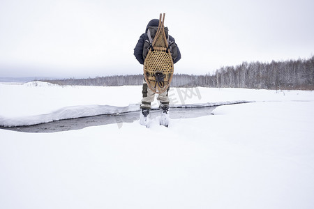 俄罗斯乌拉尔穿着传统雪鞋的中年男子在河流覆盖的雪地上的背影