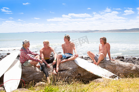 四个年轻的冲浪男性朋友在海滩岩石上聊天