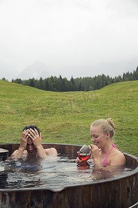 奥地利蒂罗尔萨特尔贝勒姆一对年轻夫妇在乡村热水浴缸里用玫瑰葡萄酒放松