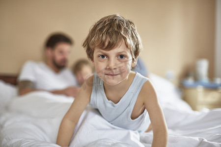 床上的男孩摄影照片_躺在父母床上的男孩微笑着看着摄像机