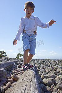 男孩在海滩上的原木上保持平衡