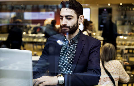 一名商人坐在咖啡馆靠窗的座位上用笔记本电脑打字