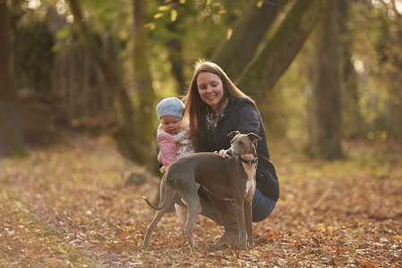 秋天公园里的中年妇女和小女儿抚摸小狗