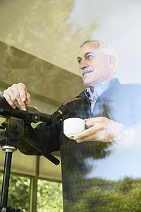 家里的老人喝着咖啡隔着窗户用望远镜