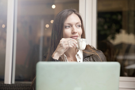 一位女商人拿着笔记本电脑在路边咖啡馆喝浓咖啡