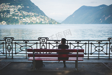 坐在公园长凳上俯瞰瑞士卢加诺湖的剪影女人的背影