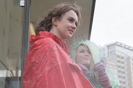 两名身穿雨衣的年轻女子在公共汽车站