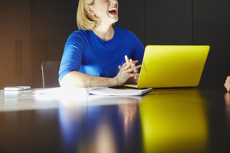 妇女坐在办公桌前拿着笔记本电脑大笑的截图