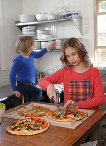 两个在柜台摄影照片_两个年轻女孩在厨房里切披萨