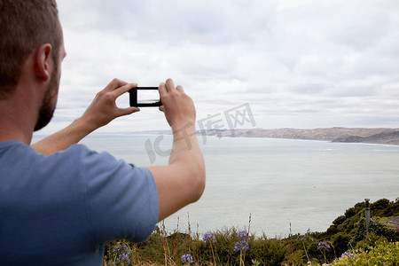 年轻男子用智能手机拍摄大海的后部剪裁