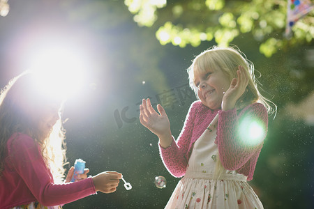 漂浮的泡泡摄影照片_两个女孩在阳光明媚的花园里吹泡泡