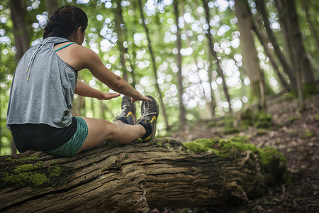 中年妇女在森林里锻炼坐在原木上伸展身体