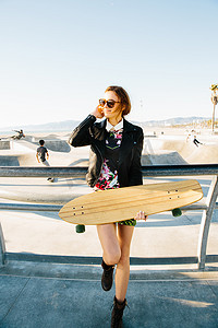 一名年轻女子站在溜冰场附近的栏杆旁手里拿着滑板