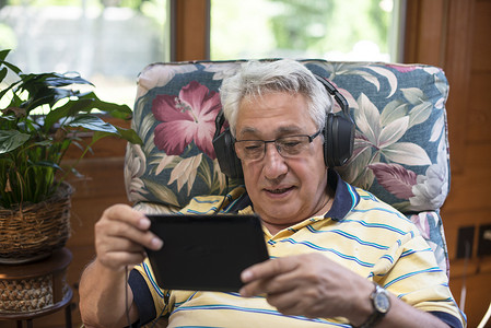 老人坐在家里戴着耳机使用数字平板电脑