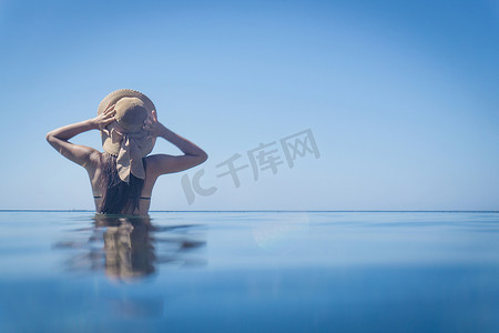 意大利撒丁岛维拉西米乌斯手戴遮阳帽站在蓝色大海中的年轻女子的后视图