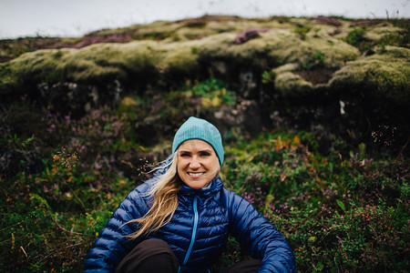 土丘摄影照片_中年妇女戴着针织帽蹲在土丘前微笑着看着镜头冰岛