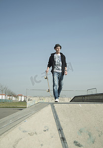 滑板坡道摄影照片_一位年轻人背着滑板穿过滑冰场