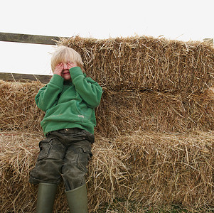 男孩把眼睛藏在干草捆上