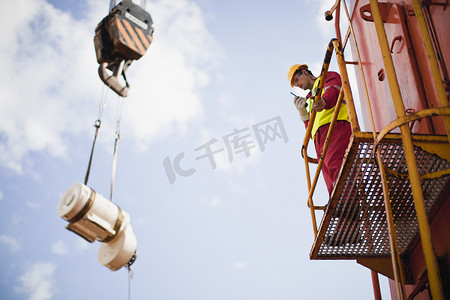 钻井工人摄影照片_石油钻井平台上的工人指挥起重机