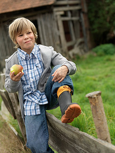 男孩吃苹果坐在栅栏上