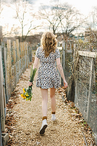 年轻女子走在户外手持向日葵后视