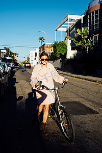 行走的女人摄影照片_美国加利福尼亚州威尼斯海滩年轻时髦的女人沿着街道推自行车