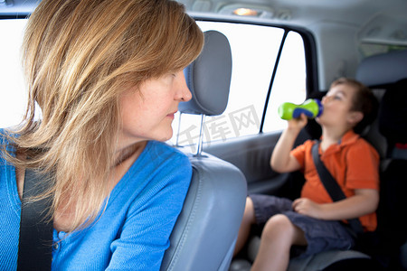 妈妈在汽车后座上看着男孩喝瓶子里的水