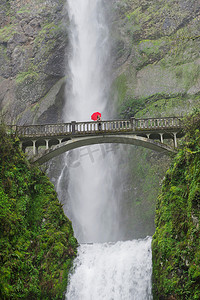 在美国哥伦比亚河峡谷马尔特诺玛瀑布上的人行桥上一名手持红色雨伞的女子