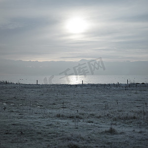诡异的纹理摄影照片_雾蒙蒙的天空中的太阳笼罩在冰冻的土地上