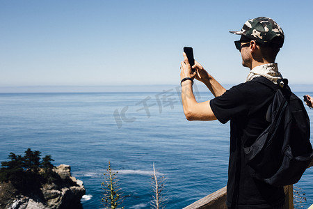 一名男子在智能手机上拍摄海景美国加利福尼亚州大苏尔