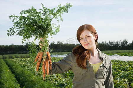 一名年轻女子在田野里拿着一串胡萝卜