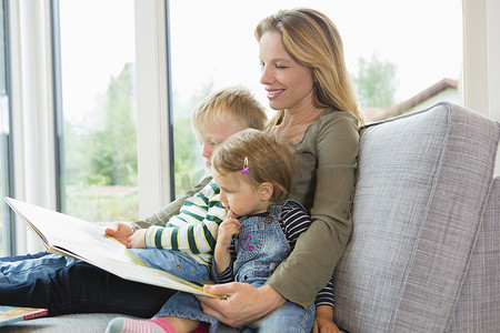 儿童培育摄影照片_母亲和两个小孩坐在沙发上看书