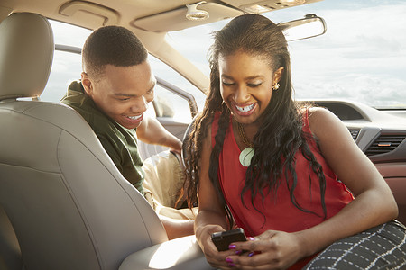 坐在车里看智能手机的年轻夫妇