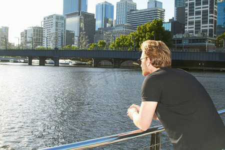 紧握扶手摄影照片_男人在桥上俯瞰城市河流