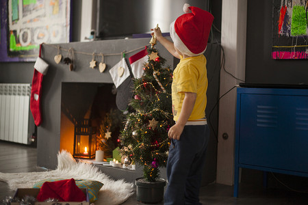 男童在壁炉前的圣诞树顶上准备装饰品