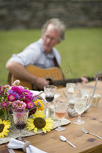 劳动系列摄影照片_桌子上放着喝了一半的饮料背景是成熟的男人弹着吉他