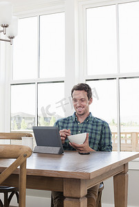 便携式摄影照片_中年男子一边吃早餐一边看着数字平板电脑