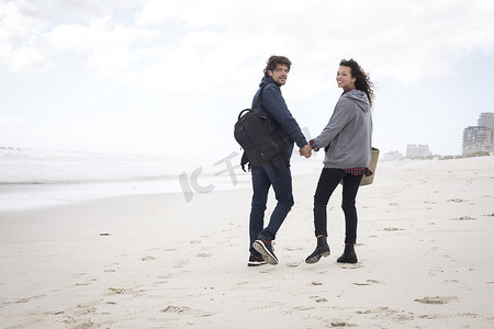 生活方摄影照片_南非西开普省海滩上散步的年轻夫妇的后视肖像