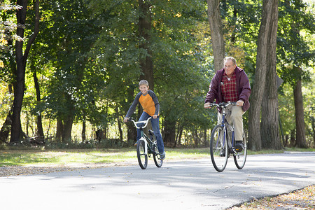 森林骑车摄影照片_老人和孙子在树林里骑车