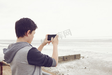 十几岁的男孩在智能手机上拍摄海洋英国埃塞克斯郡的绍森德