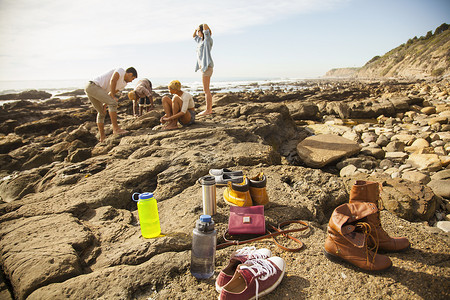 一群朋友在前台探索海滩上的岩石池塘鞋子和物品