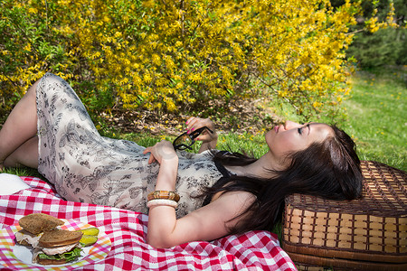 一名妇女躺在野餐毯上头枕在篮子上
