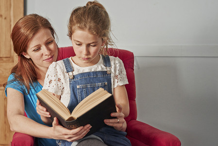 小孩儿看书摄影照片_中年妇女抱着女儿坐在扶手椅上看书