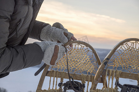 保暖衣物摄影照片_俄罗斯乌拉尔戴着手套的人准备雪地鞋的手的特写