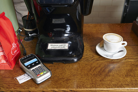 金融摄影照片_面包店柜台上的咖啡在信用卡付款机旁边