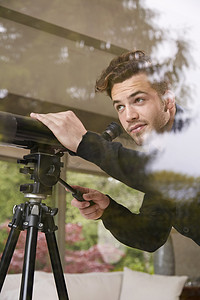 室内望向窗外摄影照片_用望远镜望向窗外的男子肖像