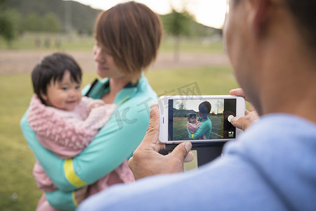 孩子给母亲摄影照片_父亲在公园里给母亲和婴儿拍照