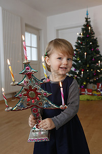 圣诞树亮摄影照片_圣诞树前拿着圣诞饰品的女孩微笑着看着镜头