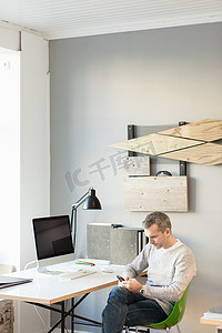 成熟的男人坐在办公室的办公桌前用智能手机低头看